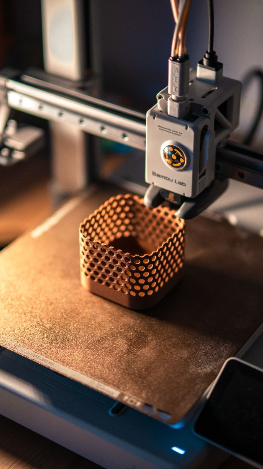 Impresora 3D fabricando una pieza con patrón de rejilla, vista de cerca durante la impresión