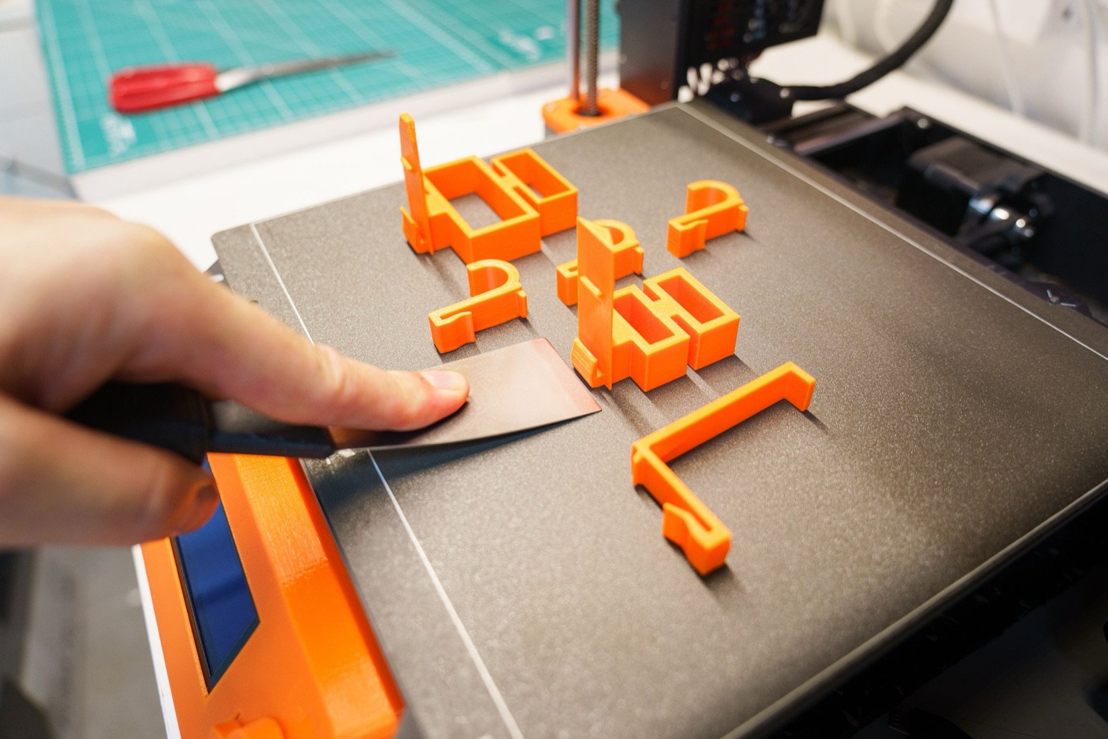 Pieza impresa en 3D siendo retirada de la cama de impresión con una espátula